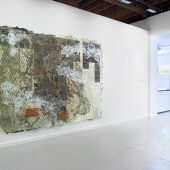 A large mixed media art piece and a man in an art gallery