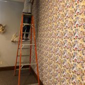 Installing the custom wallpaper A woman on a ladder trimming wallpaper