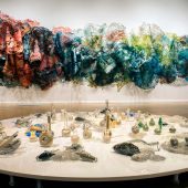 A fabric art sculpture on a wall and a display of sand in bottles